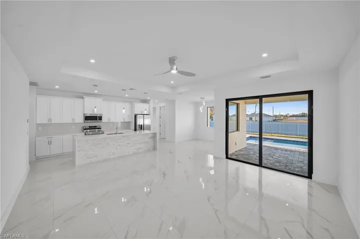 Unfurnished living room with marble finish floor, a ceiling fan, a sink, a tray ceiling, and recessed lighting