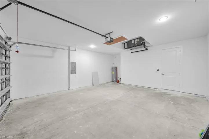 Garage featuring electric panel, a garage door opener, and electric water heater