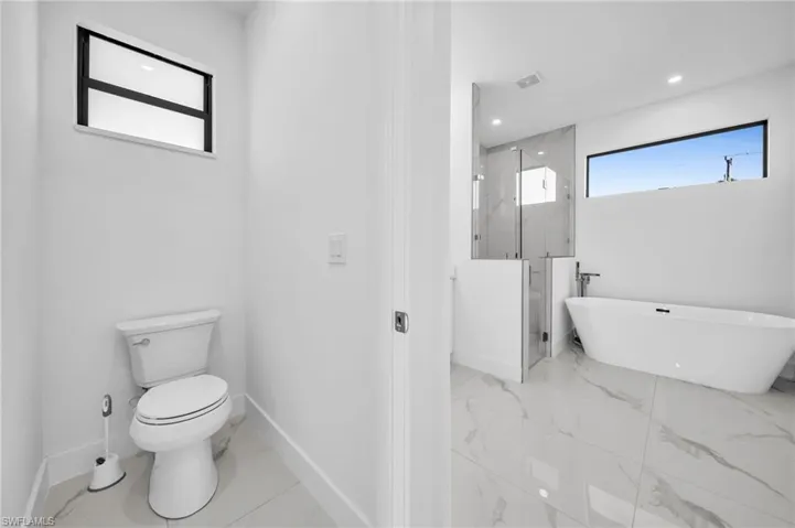 Bathroom featuring baseboards, a marble finish shower, a soaking tub, toilet, and marble finish floor