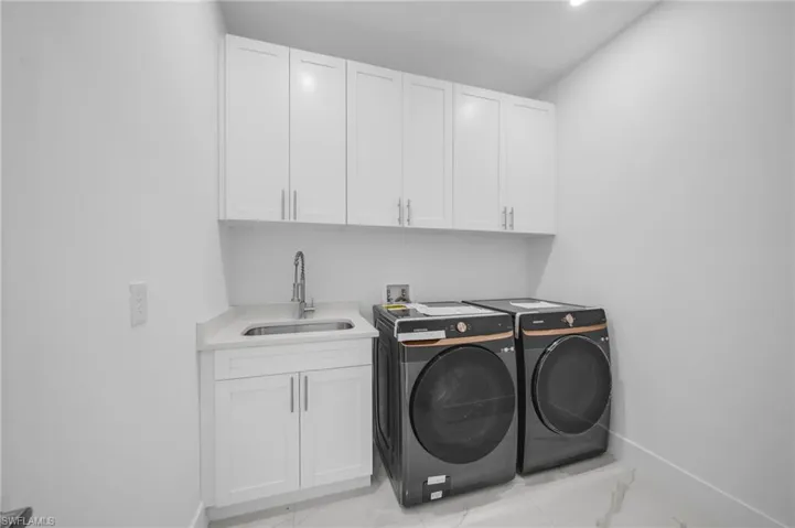 Clothes washing area with a sink, cabinet space, marble finish floor, and independent washer and dryer