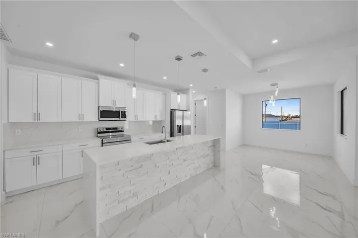 Kitchen featuring a large island with sink, white cabinets, appliances with stainless steel finishes, and a sink
