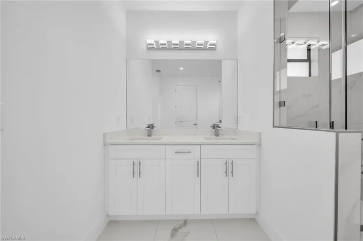 Bathroom with a marble finish shower, double vanity, baseboards, and a sink