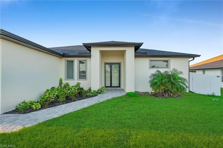 Rear view of house featuring stucco siding, a lawn, fence, french doors, and a shingled roof