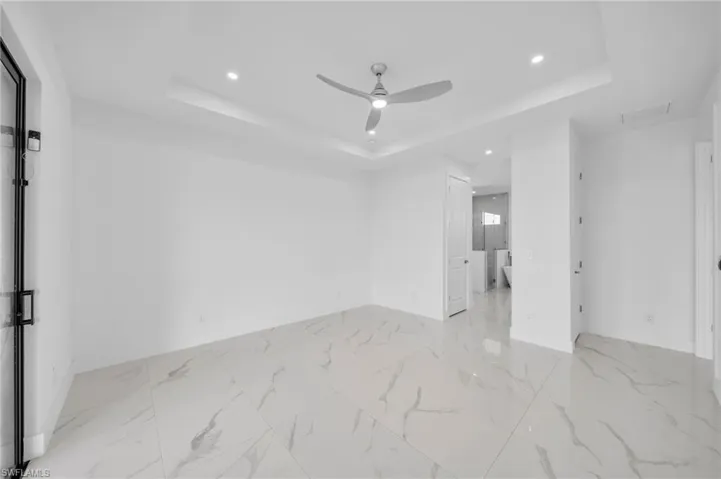 Empty room with a tray ceiling, recessed lighting, marble finish floor, and ceiling fan