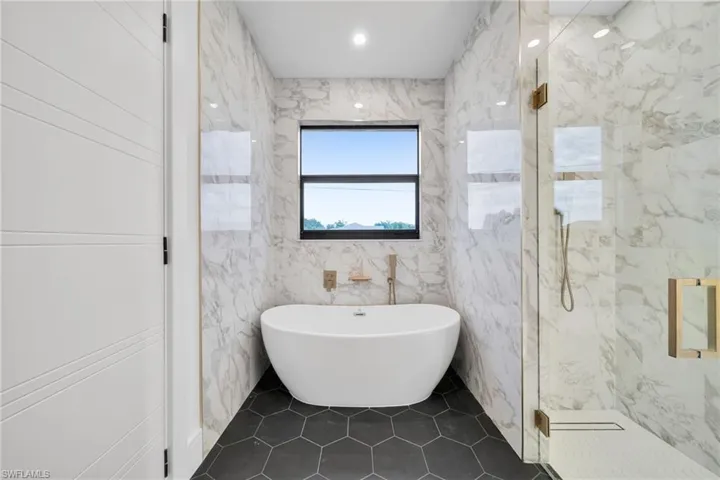 Full bathroom featuring a marble finish shower, a freestanding bath, tile walls, dark tile patterned floors, and recessed lighting