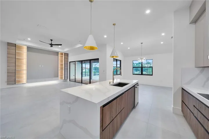 Two tone kitchen featuring open floor plan, modern cabinets, light stone counters, a center island with sink, and a raised ceiling