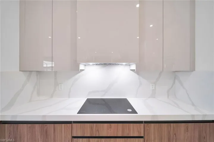 Kitchen with modern cabinets, black electric stovetop, light stone counters, and tasteful backsplash