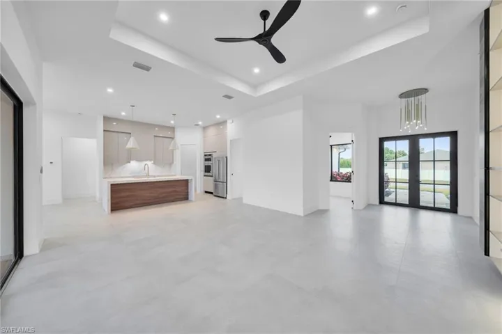 Unfurnished living room with ceiling fan, french doors, a tray ceiling, and recessed lighting