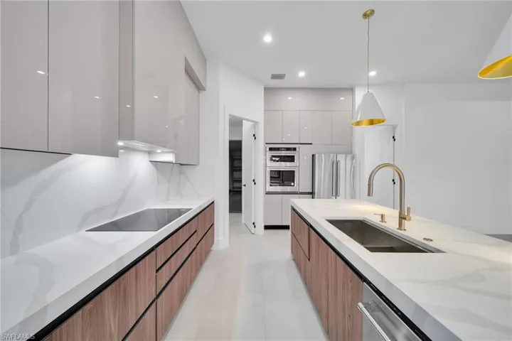 Two tone kitchen featuring modern cabinets, dual tone cabinetry, light stone countertops, stainless steel appliances, and hanging light fixtures