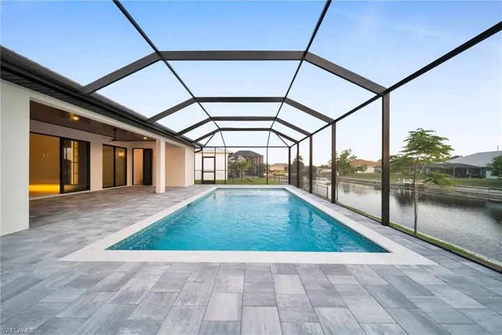 Swimming pool featuring a sunroom, glass enclosure, a water view, and a patio area