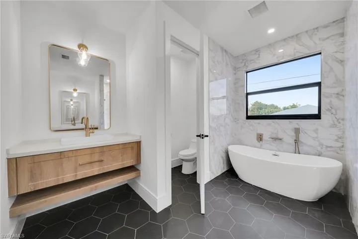 Full bathroom featuring vanity, a freestanding bath, tile walls, dark tile patterned floors, and recessed lighting