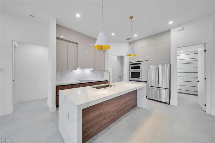 Dual tone kitchen featuring modern cabinets, two tone cabinetry, freestanding refrigerator, a kitchen island with sink, and concrete floors