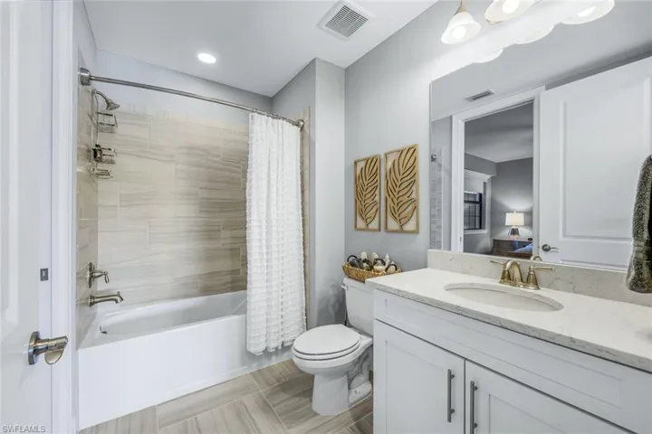 White vanity with a light-toned countertop, under-mount sink, and brass-finish faucet