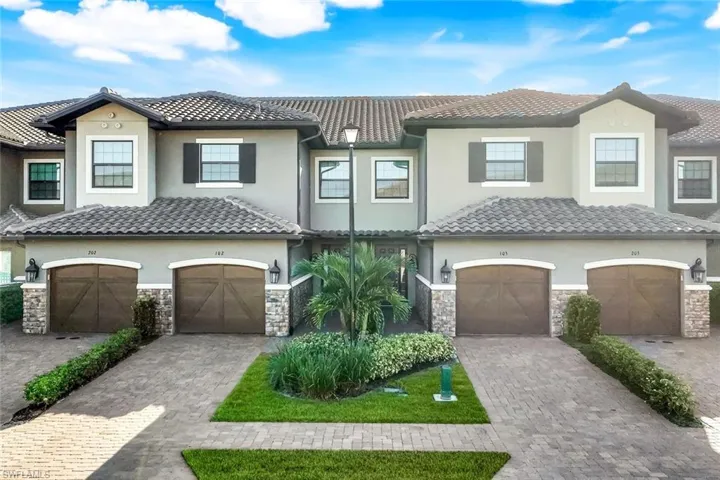 Stucco exterior with stone accents, barrel tile roof, arched garage doors, paver driveway, and exterior lighting fixtures