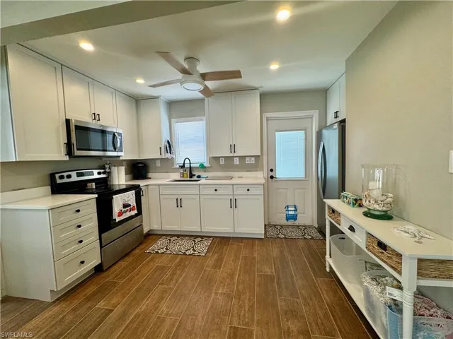 Kitchen with appliances with stainless steel finishes, white cabinetry, sink, and dark wood-type flooring