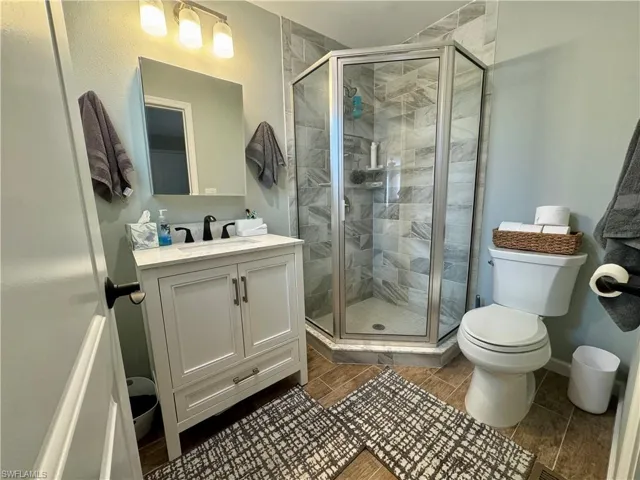 Bathroom with toilet, an enclosed shower, vanity, and wood-type flooring