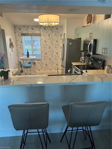 Kitchen featuring a kitchen breakfast bar, wallpapered walls, stove, a peninsula, and light stone counters