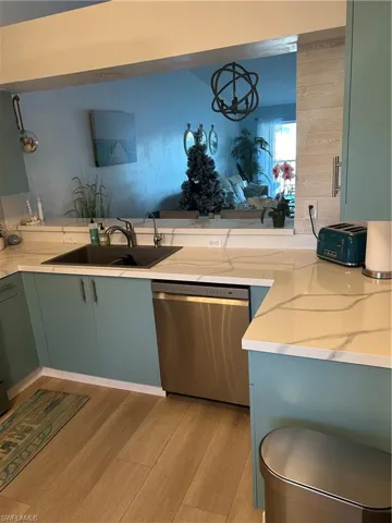 Kitchen featuring dishwashing machine, light wood-style floors, light stone countertops, and green cabinets