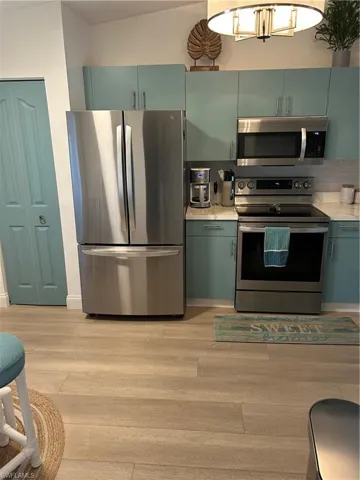 Kitchen with green cabinets, stainless steel appliances, and light wood-style flooring