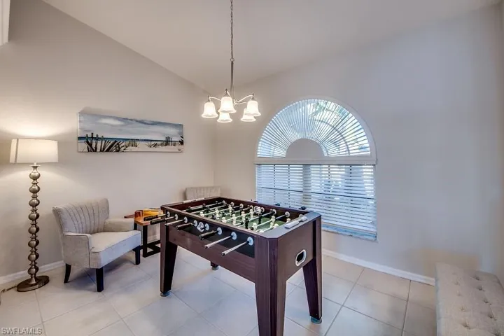 Game room with lofted ceiling, light tile patterned floors, and an inviting chandelier