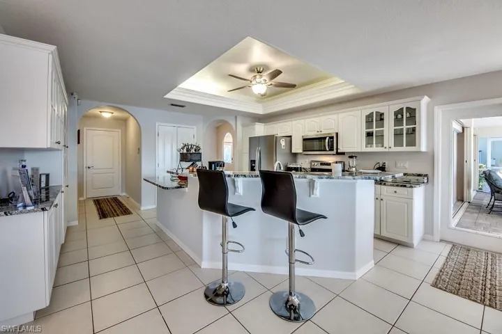 Kitchen featuring dark stone counters, white cabinets, a kitchen breakfast bar, a raised ceiling, and stainless steel appliances