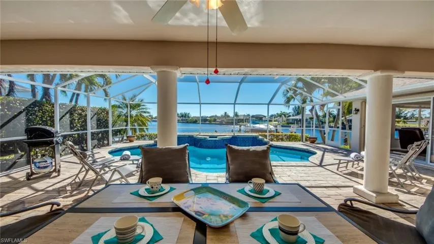 View of swimming pool with glass enclosure, a water view, a patio, and grilling area