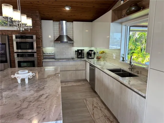 Kitchen with light stone counters, backsplash, wooden ceiling, modern cabinets, and pendant lighting