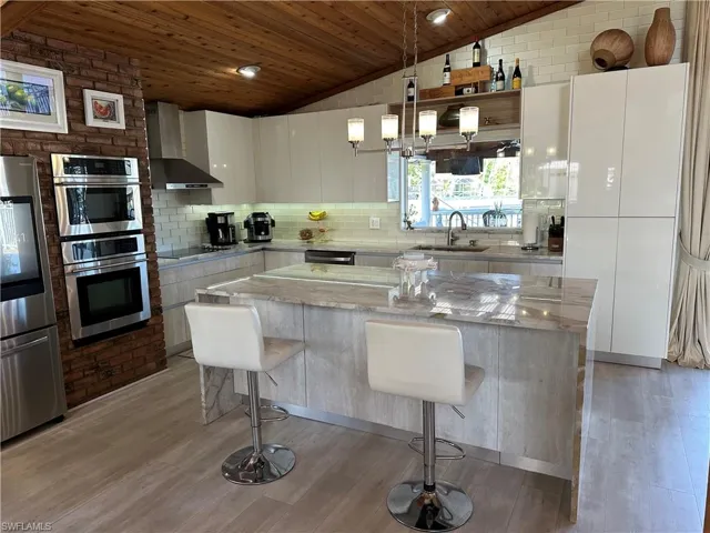 Kitchen with modern cabinets, stainless steel appliances, hanging light fixtures, light stone countertops, and decorative backsplash