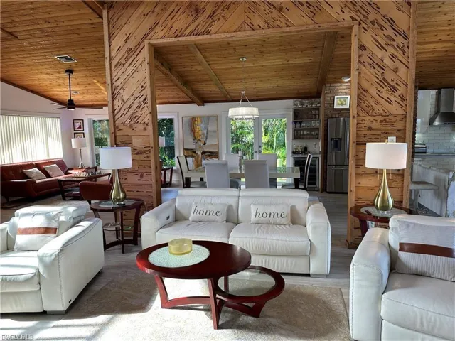 Living area with a high wood beamed ceiling, wooden walls, wood finished floors, beverage cooler, and ceiling fan