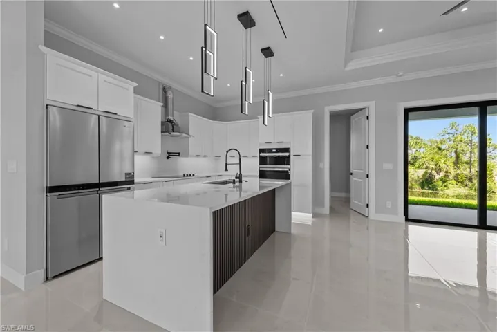 Kitchen featuring stainless steel refrigerator, a sink, wall chimney range hood, crown molding, and white cabinetry