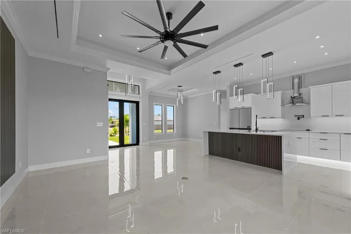 Kitchen with exhaust hood, white cabinetry, light countertops, open floor plan, and ornamental molding