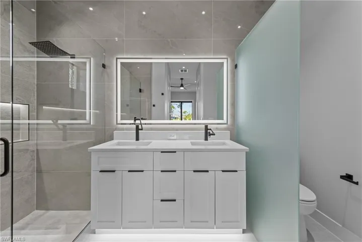 Full bath featuring a stall shower, double vanity, toilet, and baseboards
