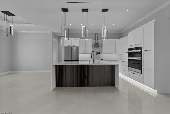Kitchen with ventilation hood, stainless steel appliances, ornamental molding, white cabinets, and an island with sink