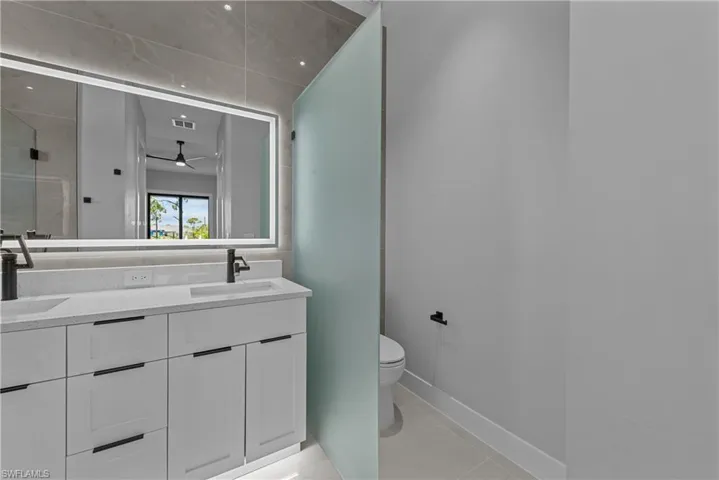 Full bath featuring toilet, double vanity, baseboards, ceiling fan, and tile patterned flooring