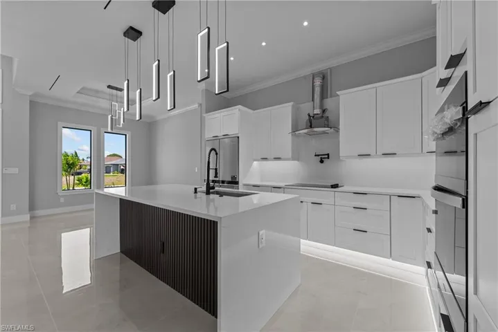 Kitchen featuring ornamental molding, an island with sink, white cabinetry, appliances with stainless steel finishes, and light countertops