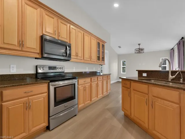 Kitchen featuring stainless-steel appliances, electric stove, microwave, dark stone countertops, glass fronted cabinets, plenty of cabinet/storage space, vaulted ceiling, and light wood finished floors