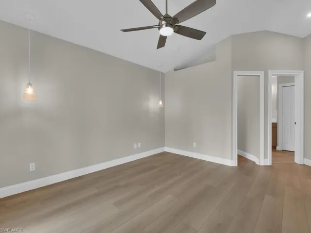Master bedroom featuring light wood-style floors, lofted ceilings with light/fan combo, walk in closet and drop pendant lighting for bedside reading.
