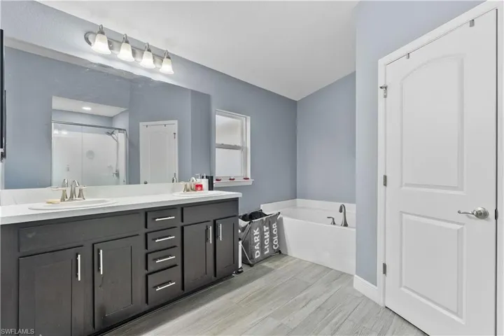 Full bathroom with a stall shower, a bath, double vanity, and light wood finished floors