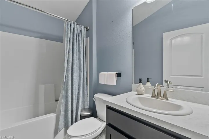 Full bathroom with vanity, shower / bath combo with shower curtain, and a textured wall