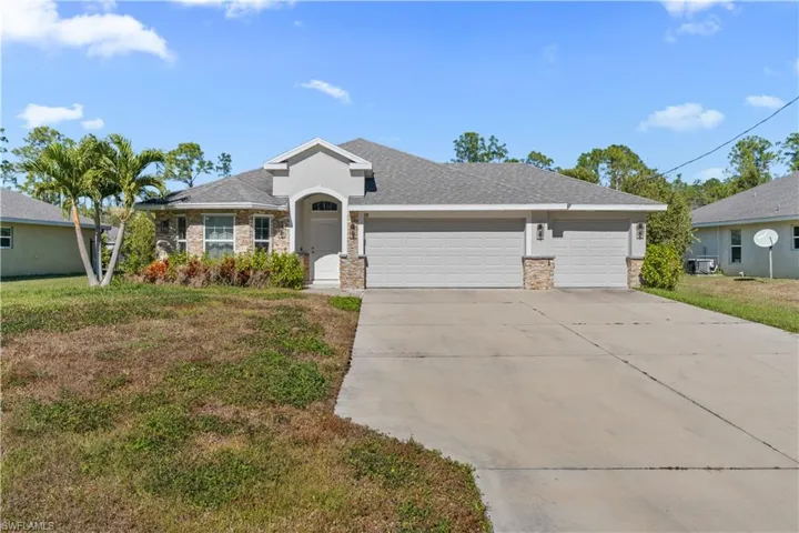 Single story home featuring an attached garage, driveway, stone siding, and a front yard