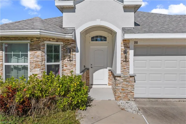 View of exterior entry featuring stone siding, an attached garage, a shingled roof, and stucco siding