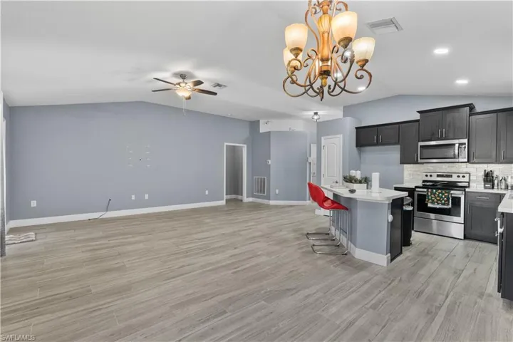 Kitchen featuring lofted ceiling, stainless steel appliances, a breakfast bar, hanging light fixtures, and a kitchen island