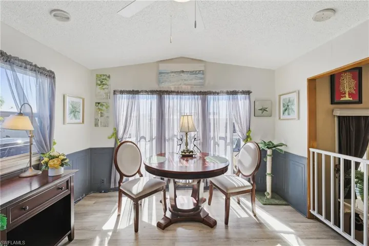 Dining room featuring a wainscoted wall, lofted ceiling, a textured ceiling, a decorative wall, and light wood-style floors