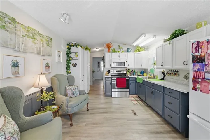Kitchen with vaulted ceiling, white cabinets, white appliances, light countertops, and light wood-type flooring