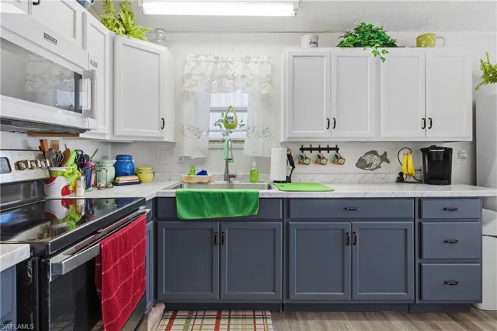 Kitchen featuring stainless steel electric range oven, white cabinetry, white microwave, light wood finished floors, and gray cabinetry