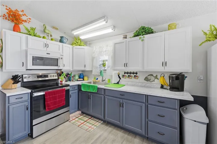 Kitchen featuring stainless steel electric range, white cabinets, white microwave, a textured ceiling, and light wood-style flooring