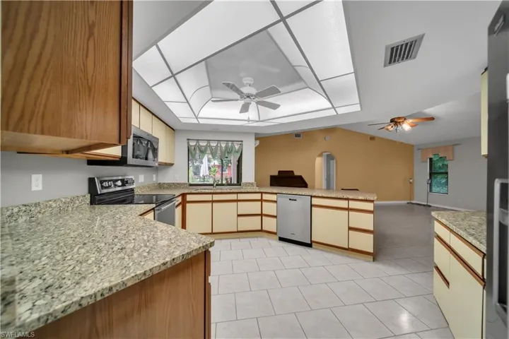 Kitchen featuring appliances with stainless steel finishes, light stone counters, brown cabinetry, and light tile patterned floors