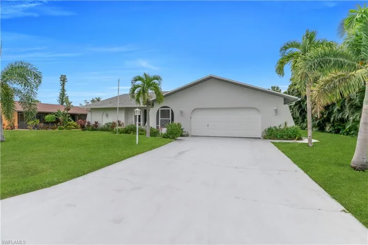 Ranch-style home featuring an attached garage, a front lawn, driveway, and stucco siding