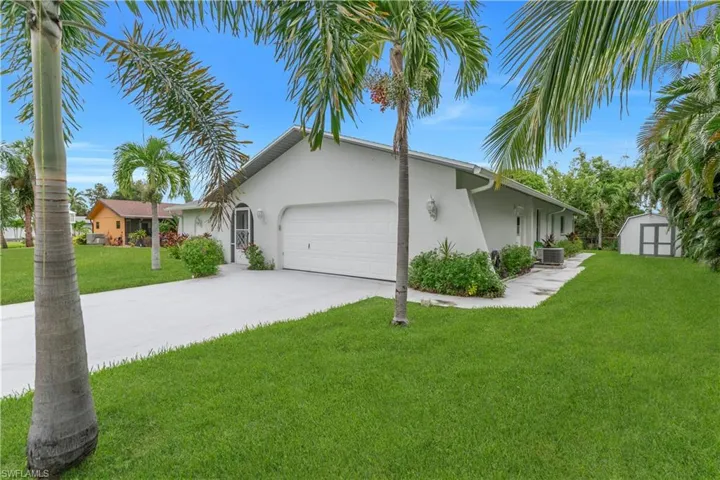 View of property exterior with stucco siding, a garage, a lawn, concrete driveway, and a storage shed