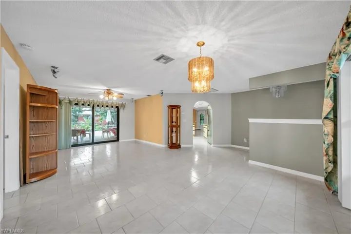 Spare room featuring arched walkways, light tile patterned floors, ceiling fan, a textured ceiling, and a chandelier